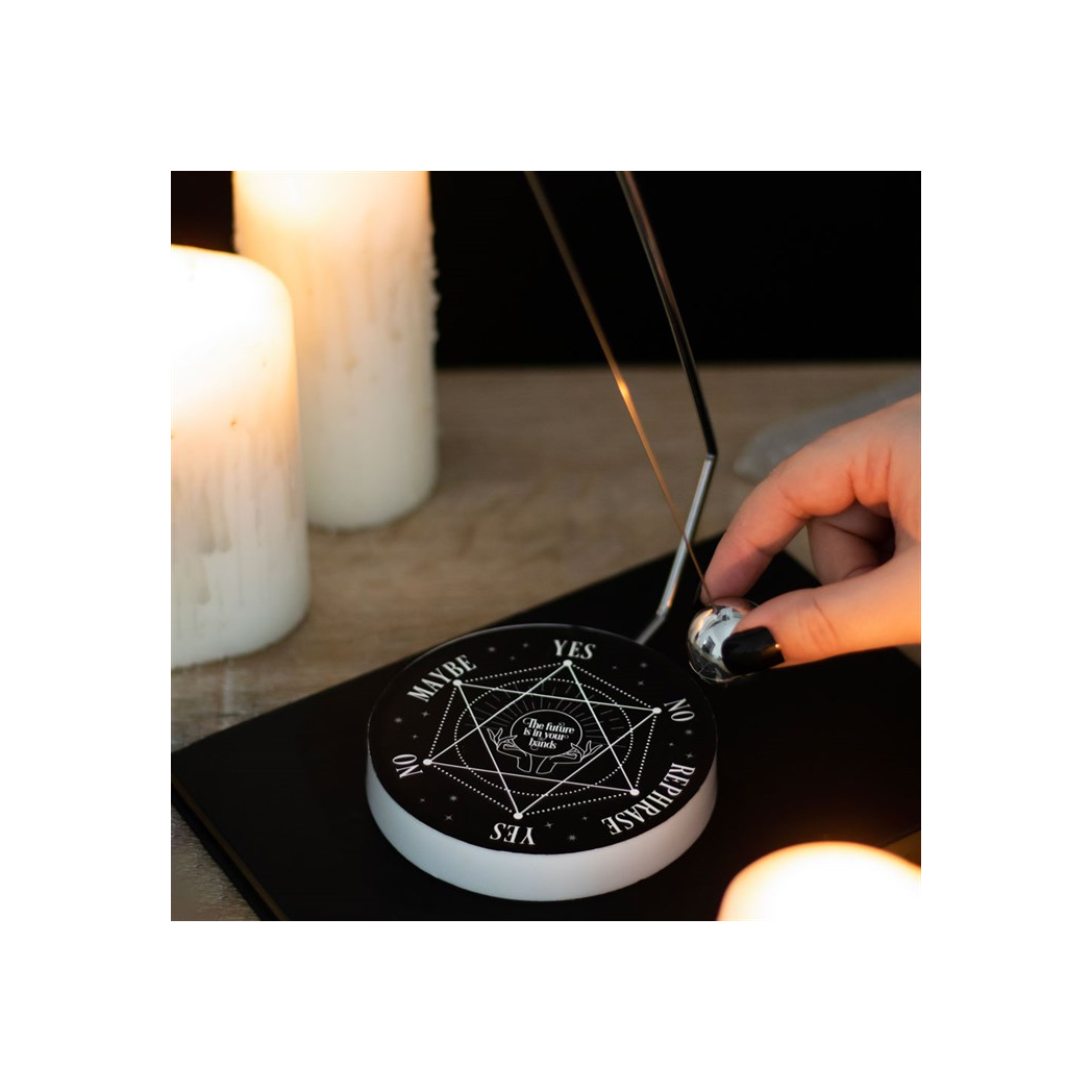 Hand using a dowsing rod on a black crystal grid with candles in the background