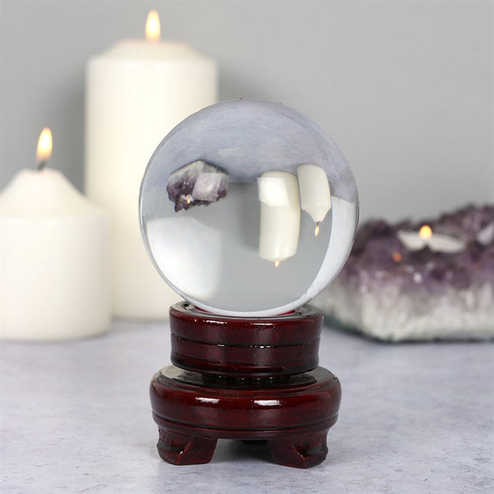 Crystal ball with amethyst inside on a wooden stand with candles and crystal rock in the background