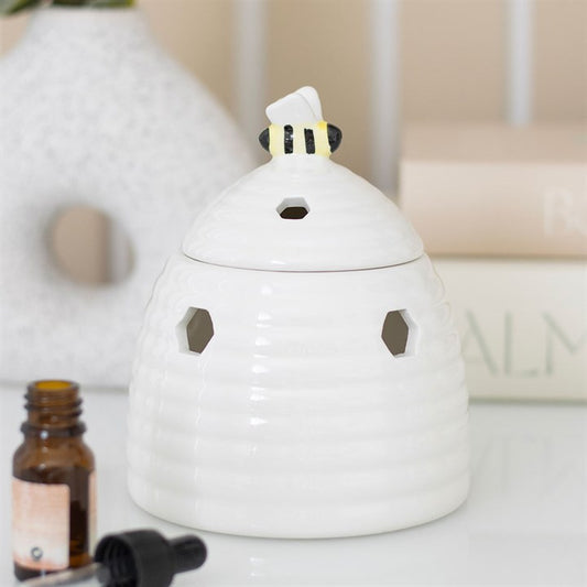 White ceramic diffuser with a small figurine on top, next to an essential oil bottle, on a light surface.