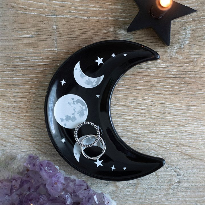 Black crescent moon-shaped dish with moon phases and stars on a wooden surface.