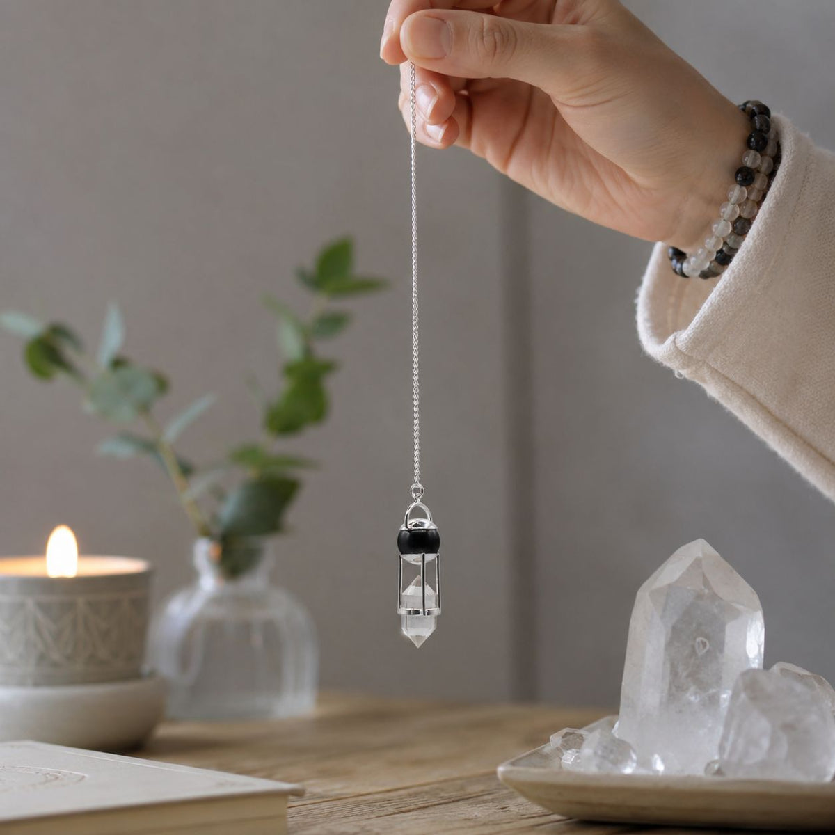 Hand holding a crystal pendant with a candle and crystals in the background