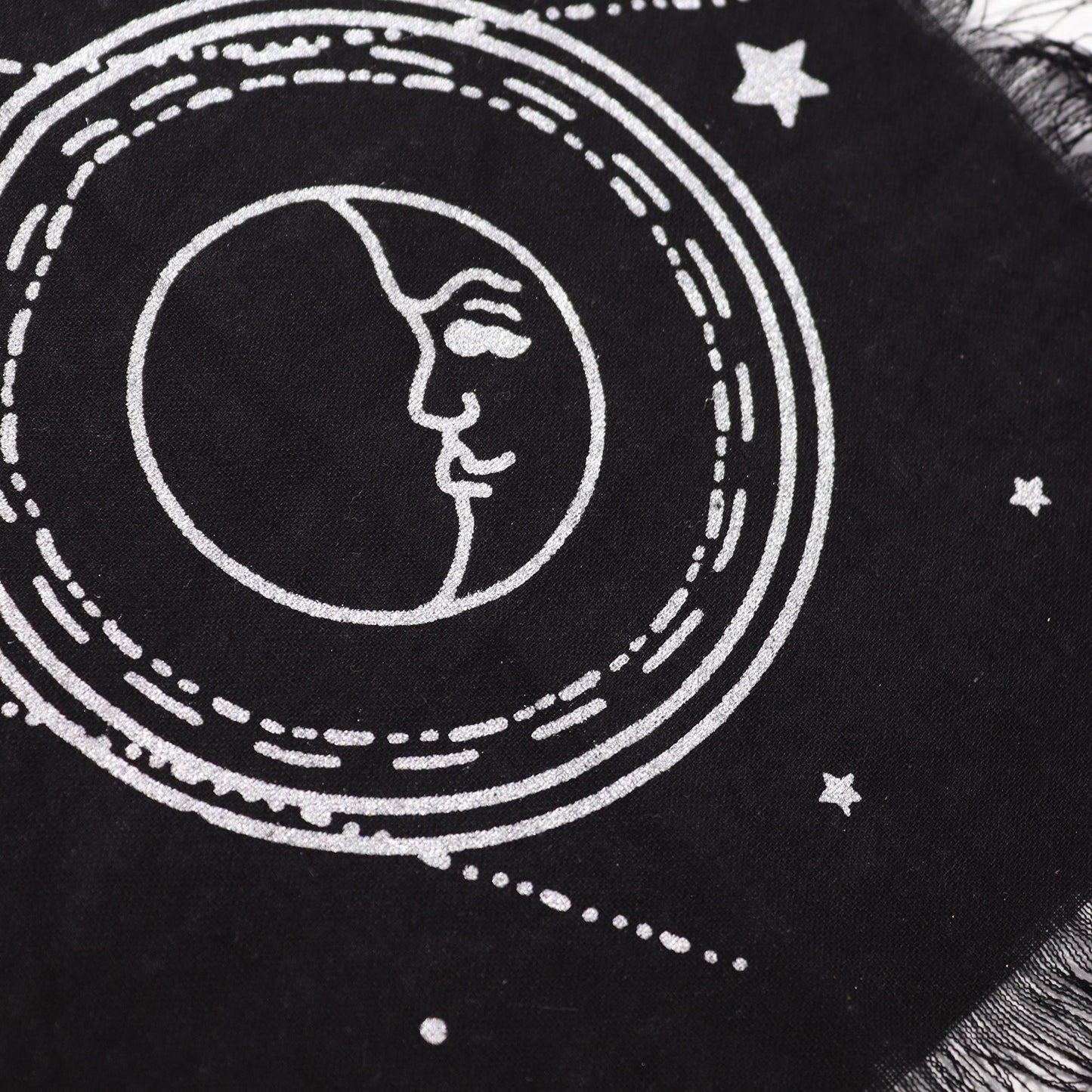 Black fabric with white embroidered design of a face within a circular pattern and stars.