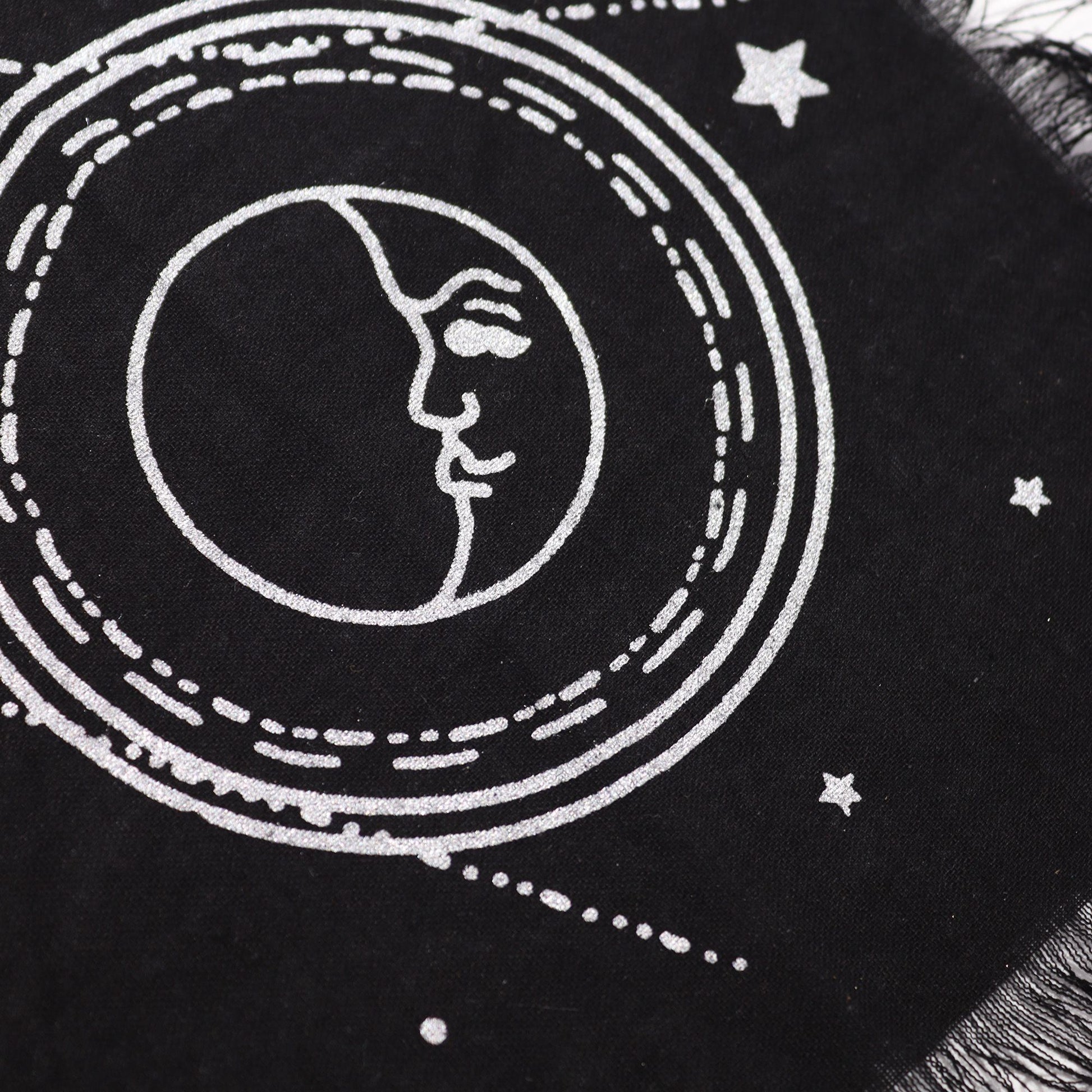 Black fabric with white embroidered design of a face within a circular pattern and stars.