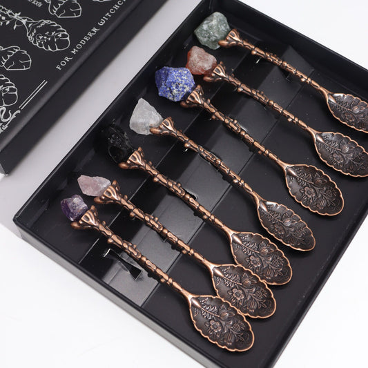 Set of decorative spoons with engraved designs in a black box, featuring crystals on top.