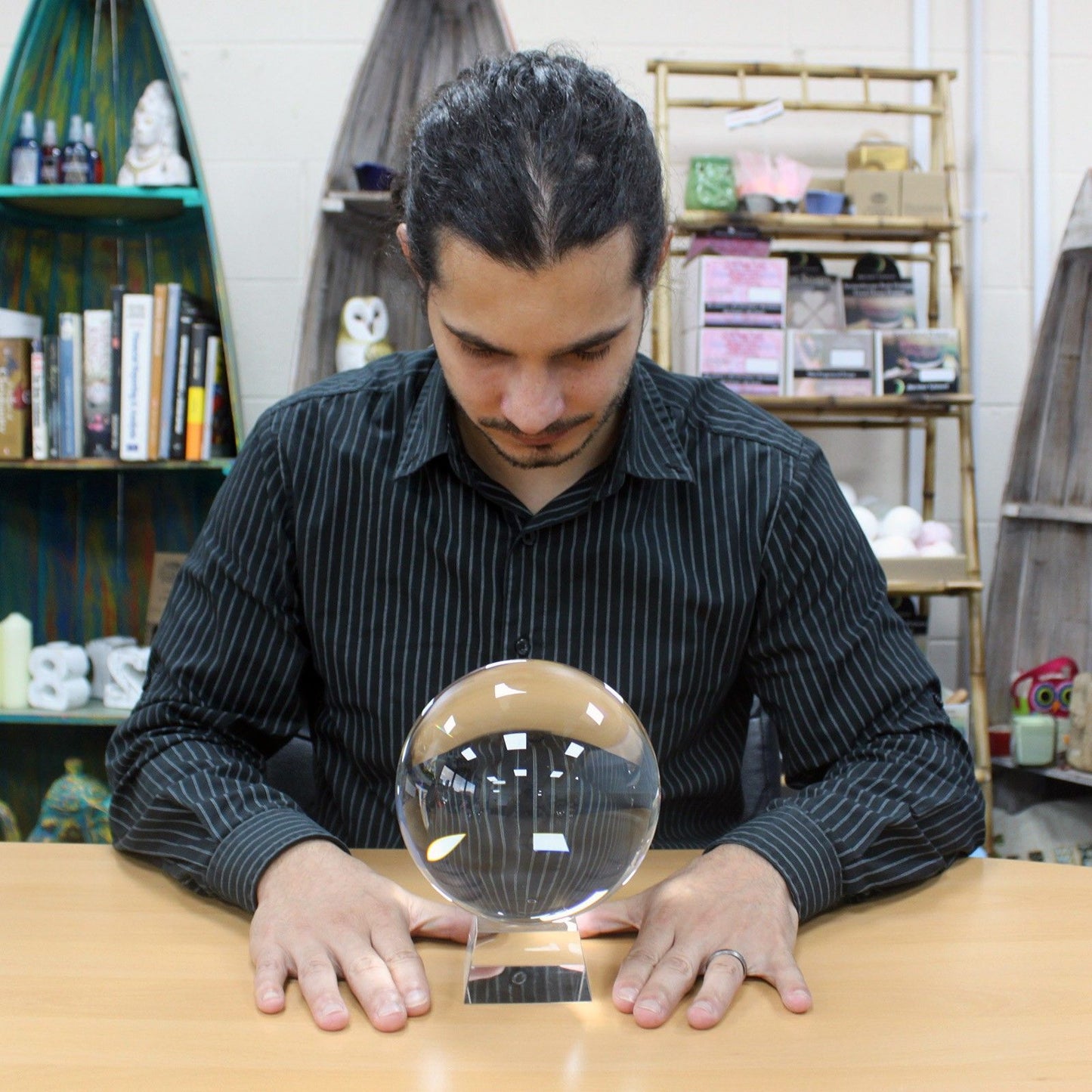 Man interacting with a crystal ball on a table in a room with shelves and books.