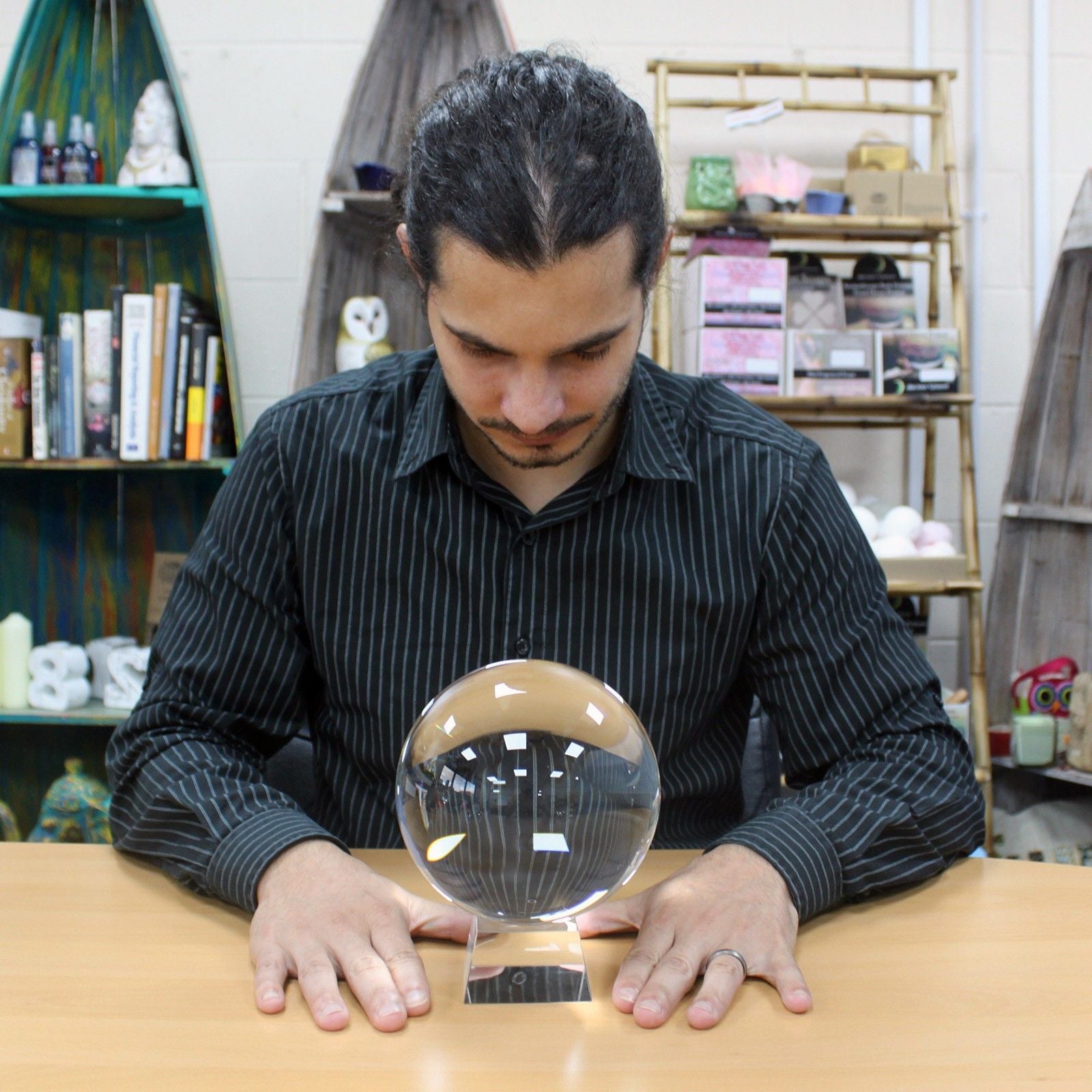 Man interacting with a crystal ball on a table in a room with shelves and books.