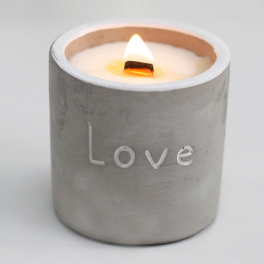 Cement candle holder with 'Love' engraving and lit candle on a light gray background