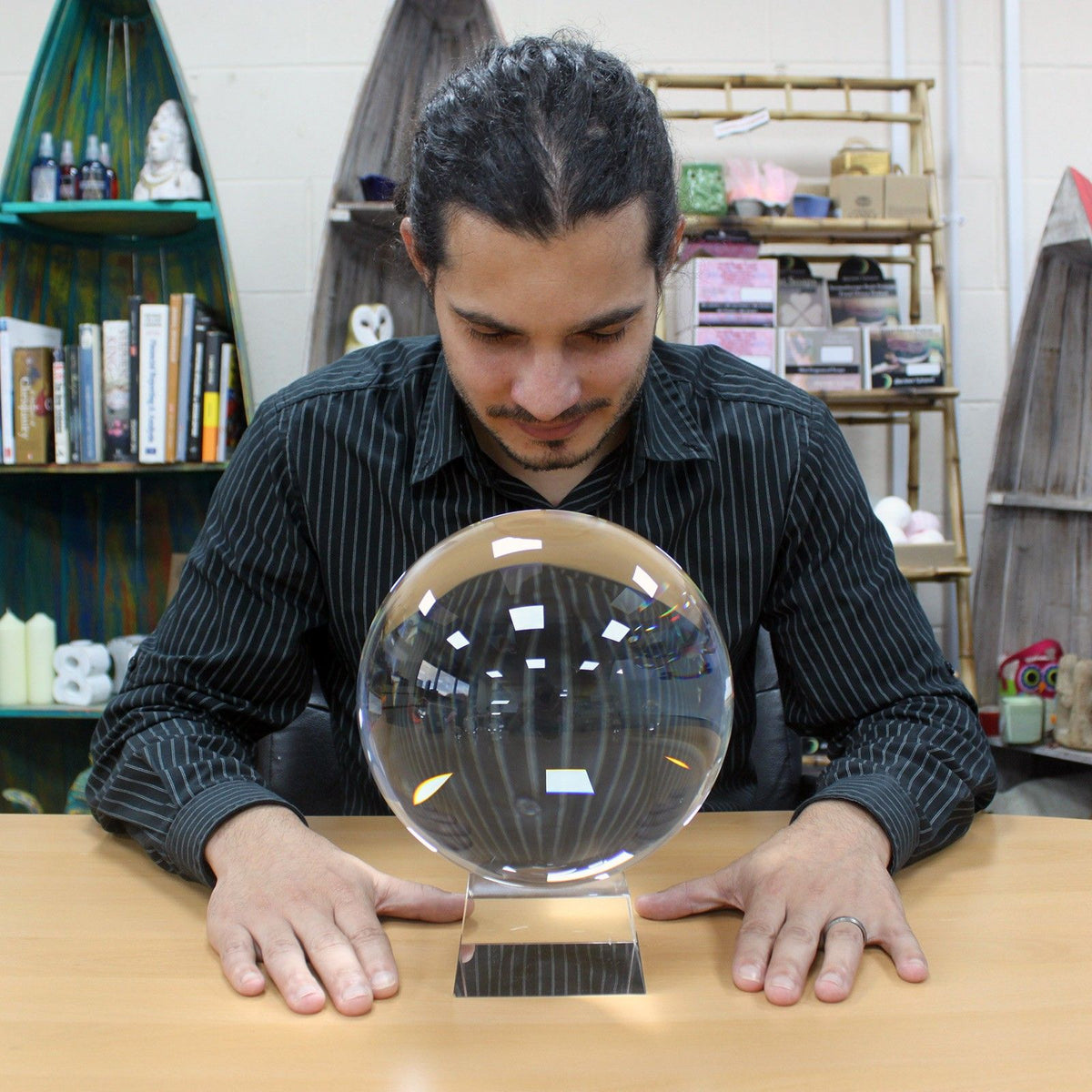 Man examining a large crystal ball on a table with shelves in the background