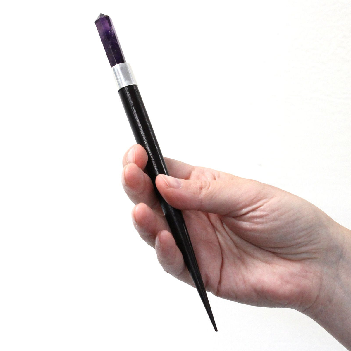 Hand holding a black and silver  wand with a purple crystal top on a white background