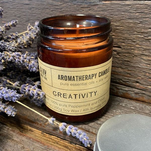Aromatherapy candle labeled 'Creativity' with lavender flowers on a wooden surface