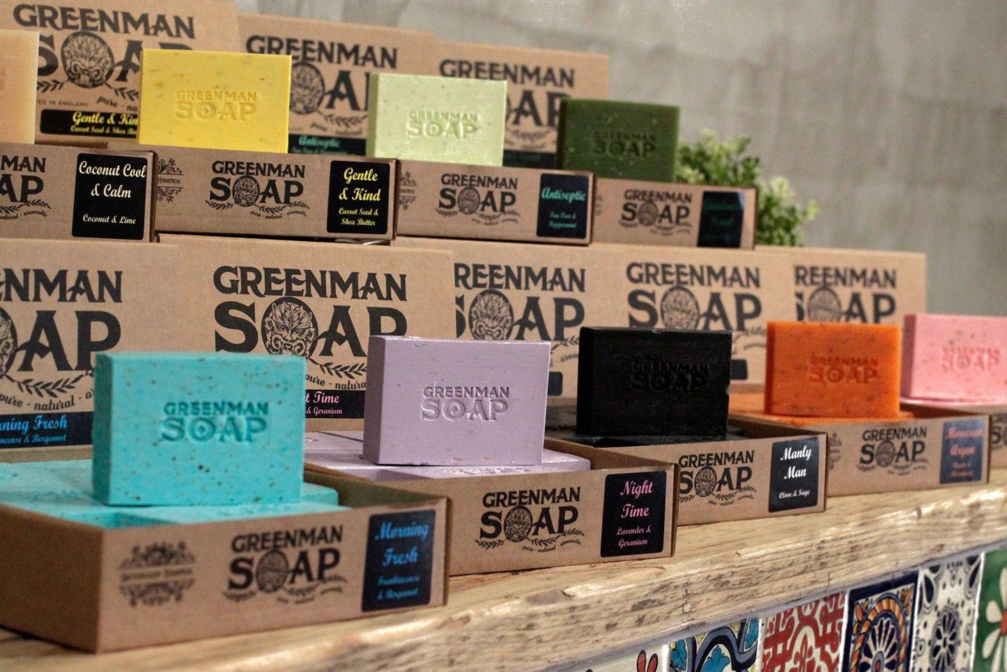 Display of Greenman Soap bars and packaging on a wooden shelf.