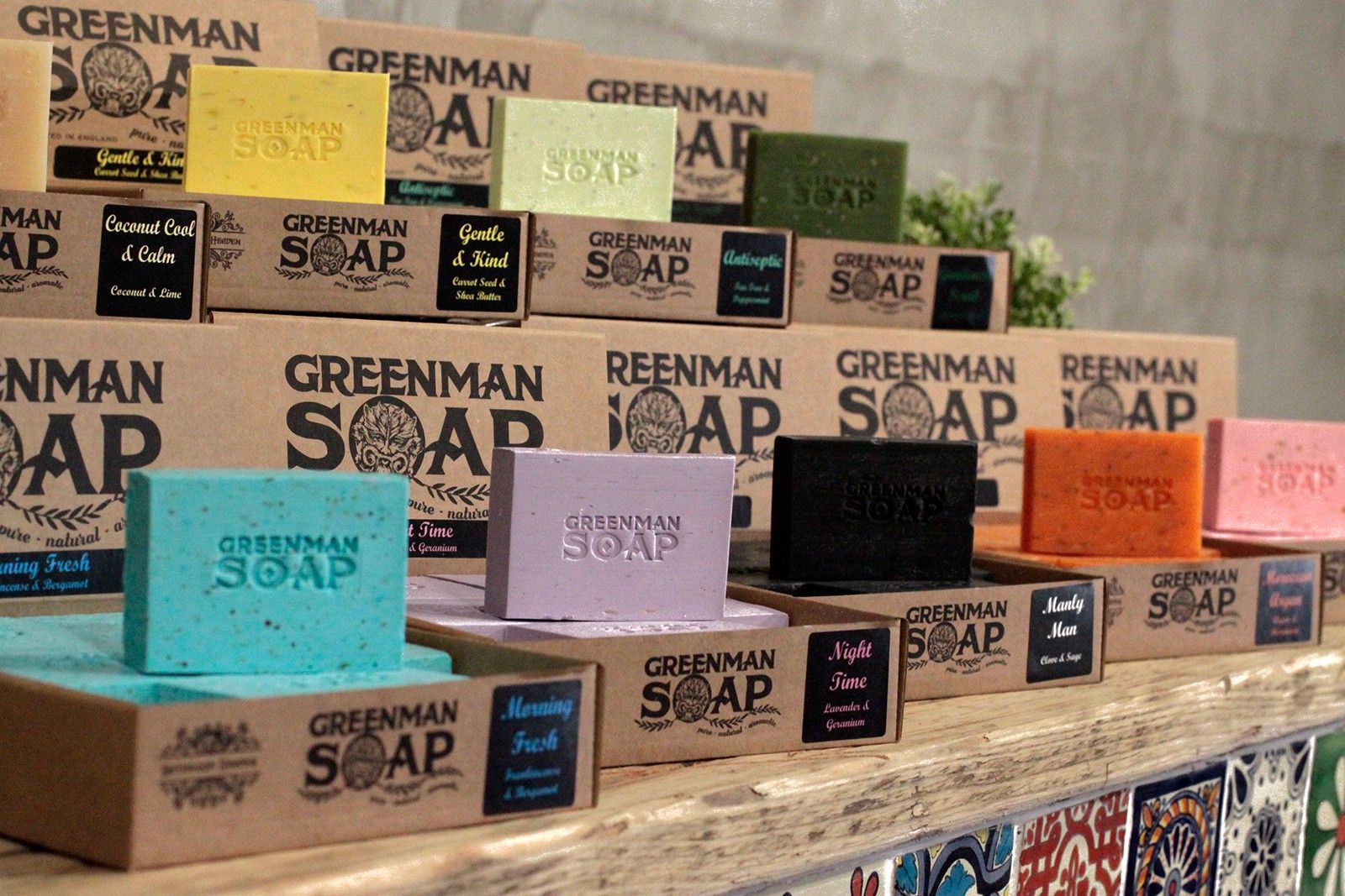 Display of Greenman Soap bars and packaging on a wooden shelf.