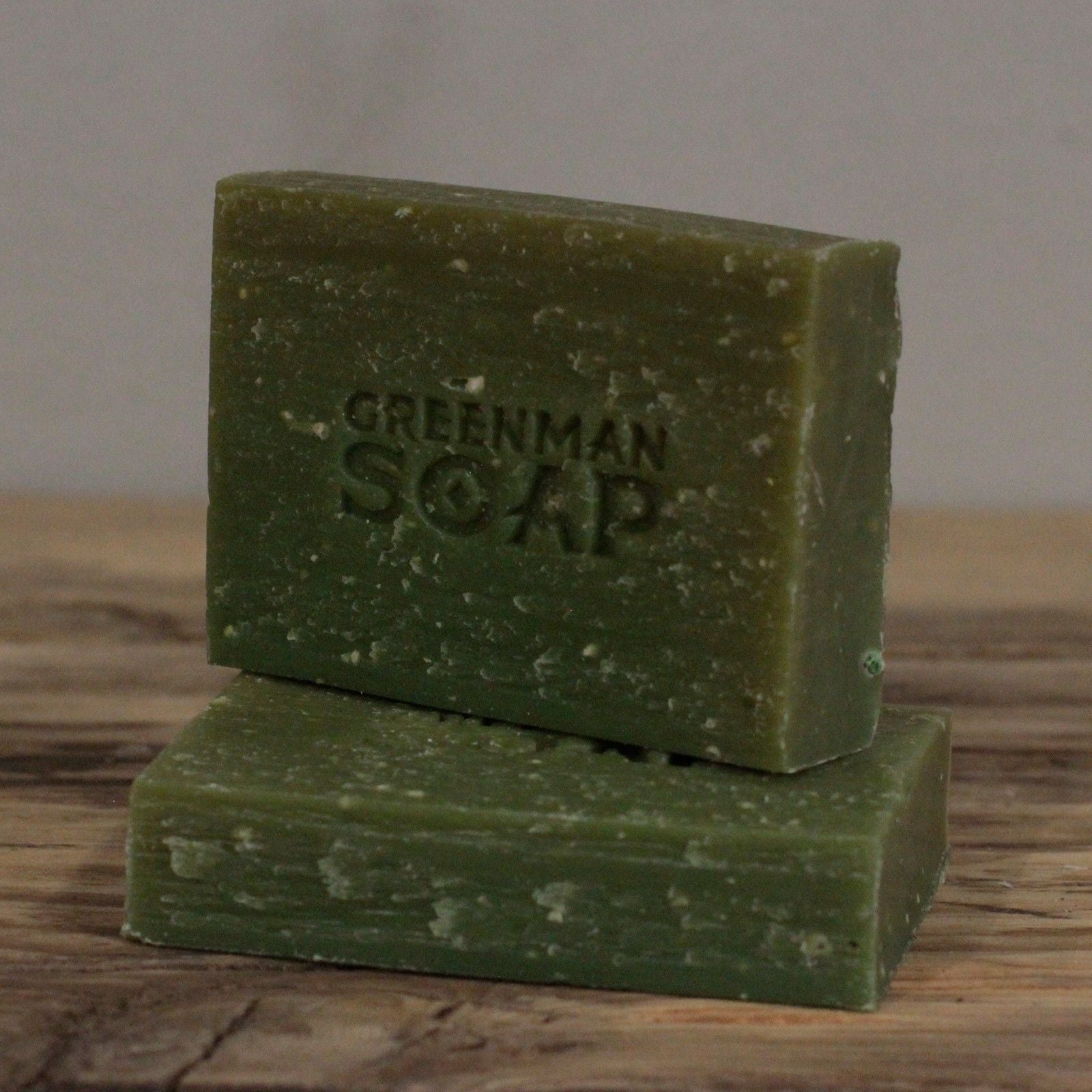 Two green bars of soap with 'Greenman Soap' branding on a wooden surface.
