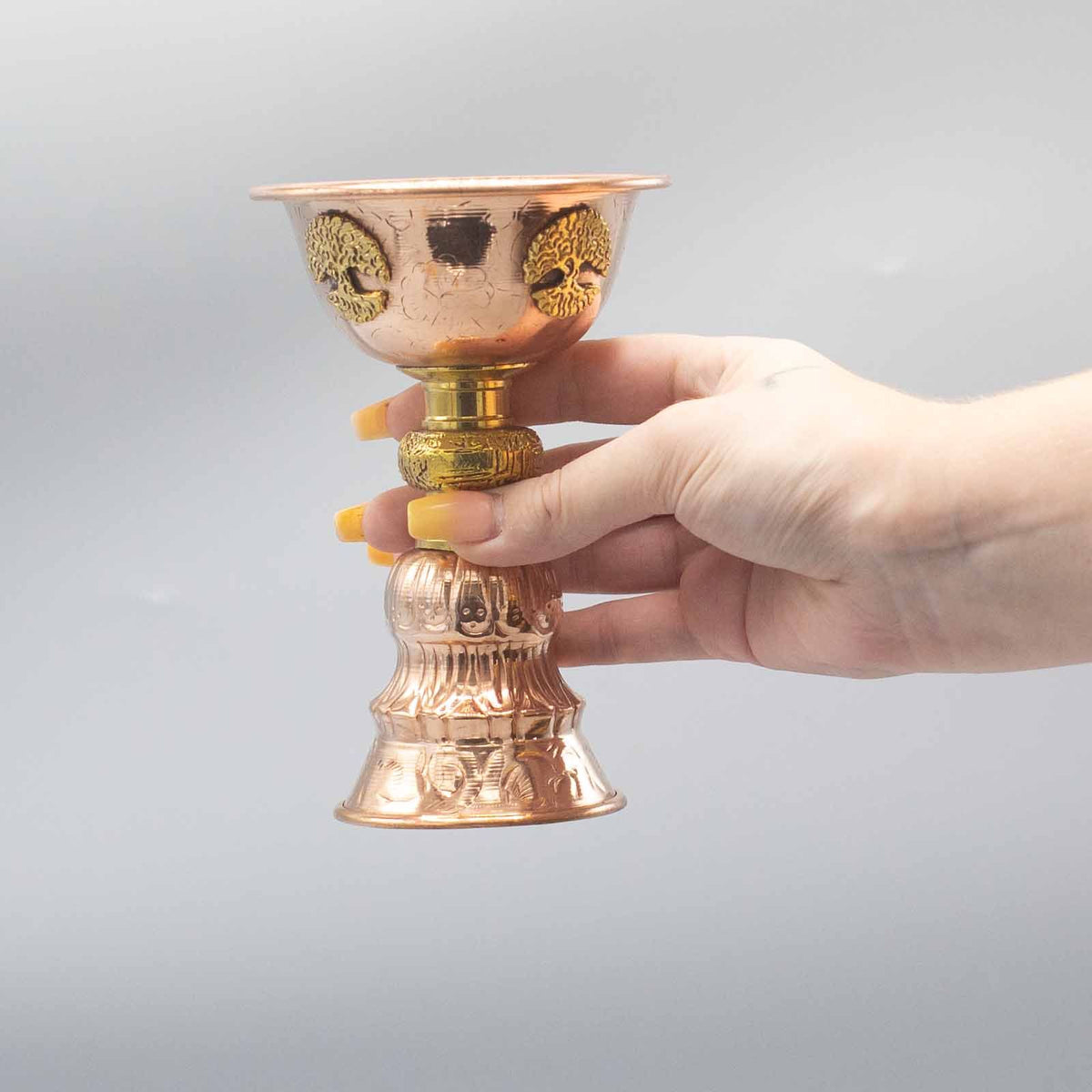 Hand holding a copper and gold decorative cup against a gray background